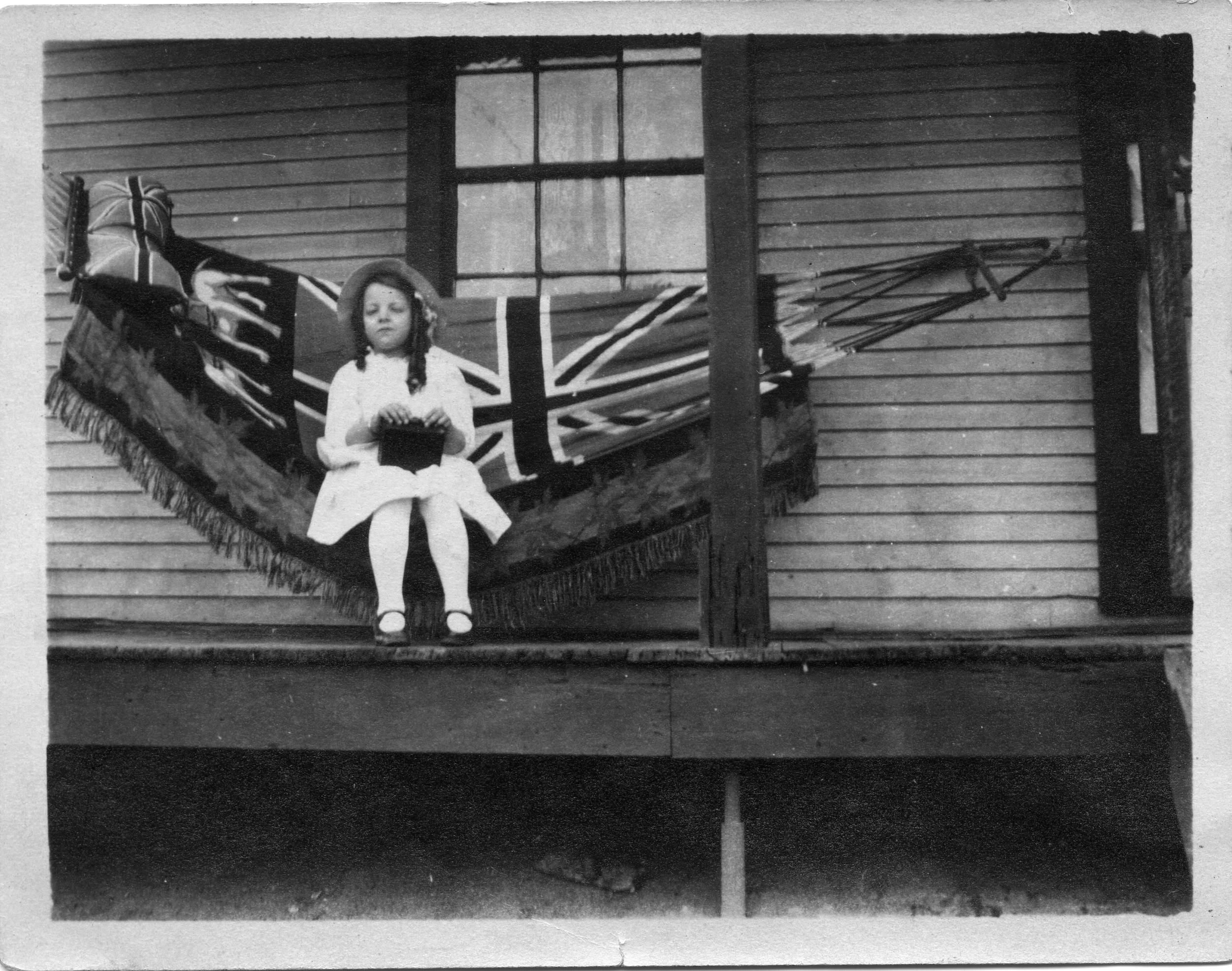 A child sitting in a hammock on a porch.